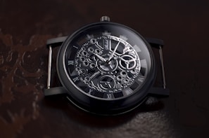A detailed view of a mechanical watch showcasing intricate gears and Roman numerals on a dark, reflective background. The watch face is ornate with visible cogs and hands indicating time.
