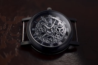 A detailed view of a mechanical watch showcasing intricate gears and Roman numerals on a dark, reflective background. The watch face is ornate with visible cogs and hands indicating time.