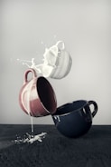 white mug spilling milk on brown and black mugs