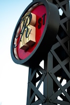 A circular sign with large, stylized letters in the center placed on a lattice-like metal framework. The background of the sign is red, with letters 'RH' prominently displayed. The letters 'ST' appear smaller on the side. The structure has a modern industrial design.