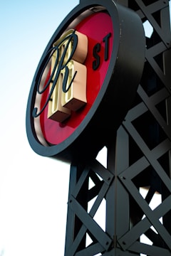 A circular sign with large, stylized letters in the center placed on a lattice-like metal framework. The background of the sign is red, with letters 'RH' prominently displayed. The letters 'ST' appear smaller on the side. The structure has a modern industrial design.