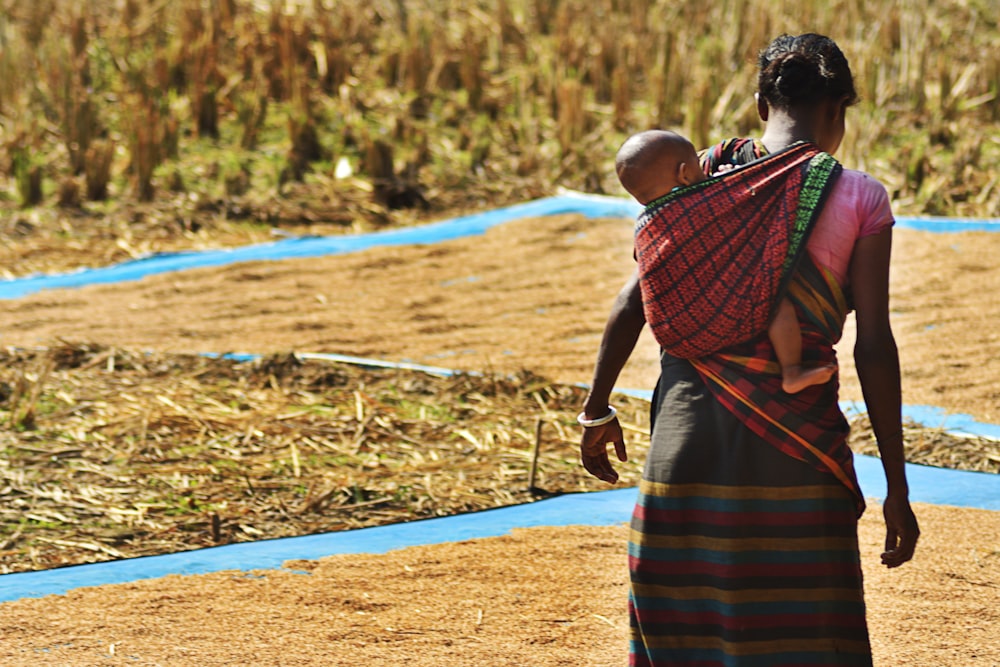 woman carrying child through sling while drying seeds