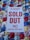 A white sign with bold red text stating 'EVENT SOLD OUT NO PARKING REFUNDS' is placed on a colorful sequined surface composed of blue, red, gold, and silver circular patterns.