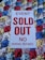 A white sign with bold red text stating 'EVENT SOLD OUT NO PARKING REFUNDS' is placed on a colorful sequined surface composed of blue, red, gold, and silver circular patterns.