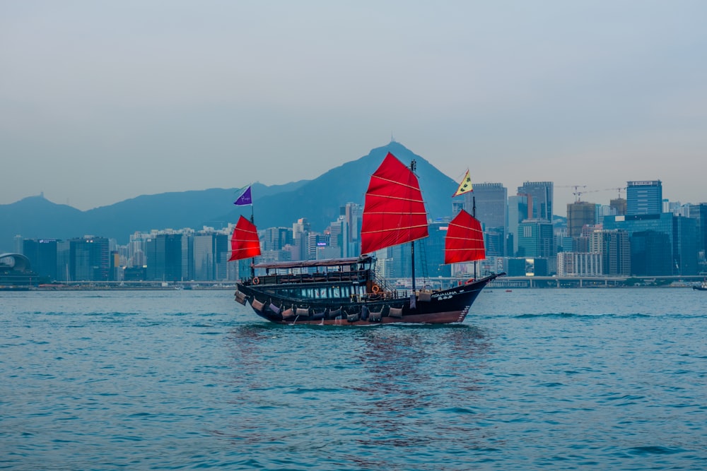 junk sailing ship in sea in front of buildings under gray sky