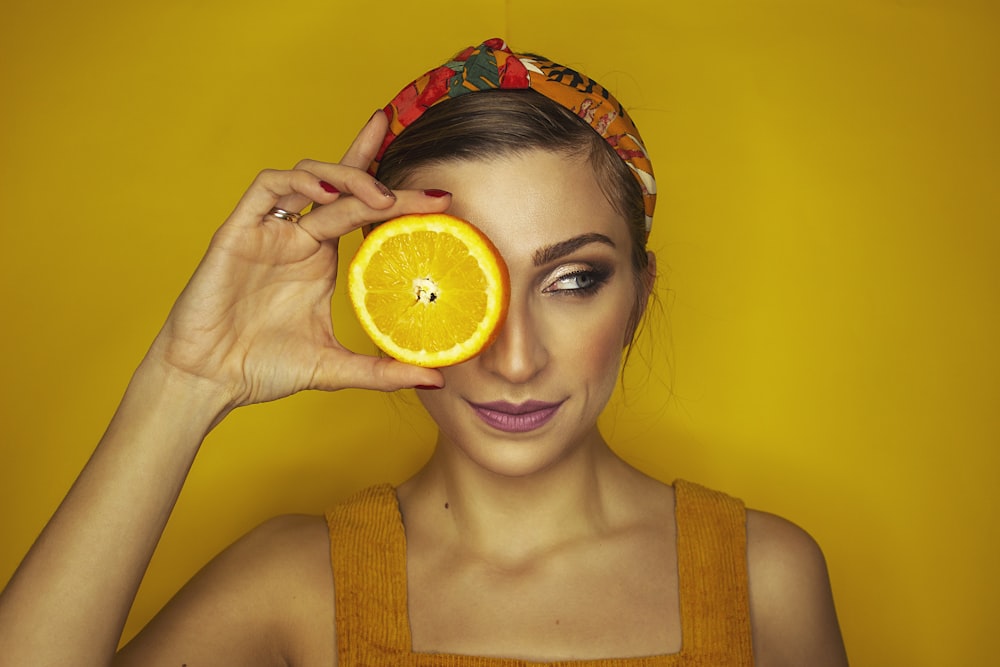 Mujer cubriendo su ojo derecho con una rodaja de naranja