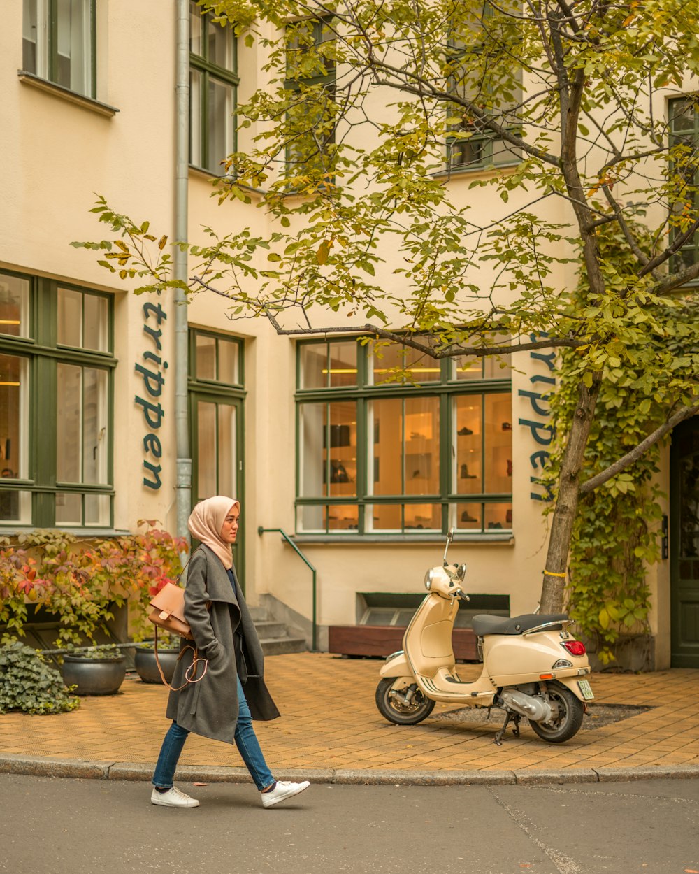 woman in black jacket walking near gray motor scooter