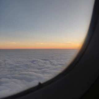 A calm sunrise view from an airplane window showing soft clouds below.