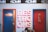 Two restroom doors are side by side, one painted blue with a red frame and another red with a blue frame. Above each door are skateboard decks mounted horizontally. The word 'restrooms' is prominently painted in large, bold letters in a pink and white 3D style between the doors. A paper towel holder can be seen inside the blue door that is slightly ajar. The top part of the wall displays the text '4DWN' repeatedly.