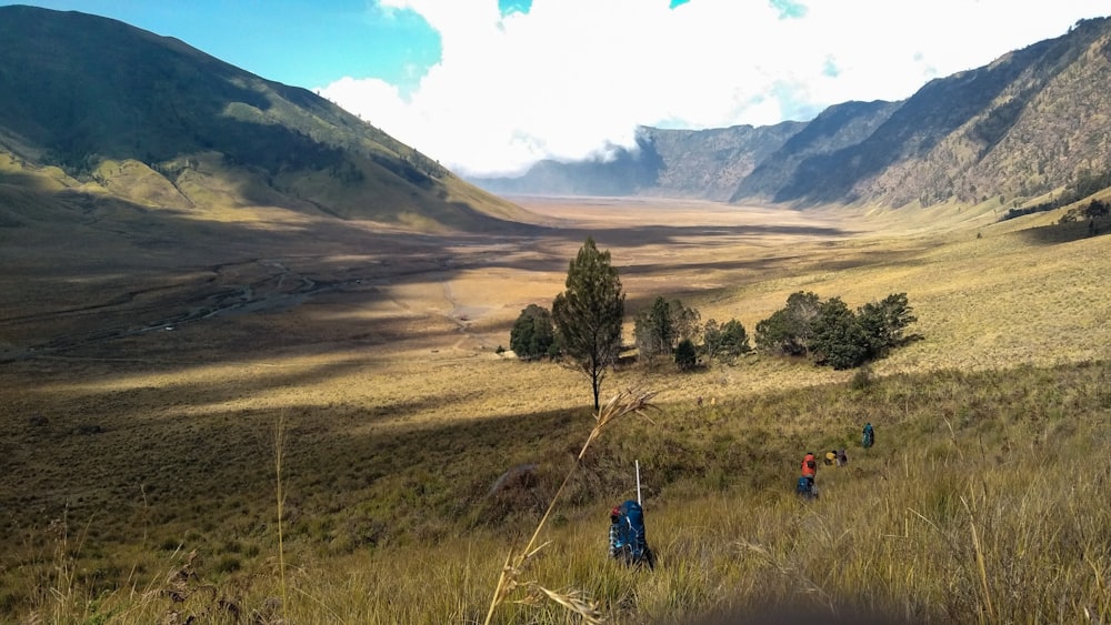 aerial photography of people hiking on field viewing mountain under white and blue sky