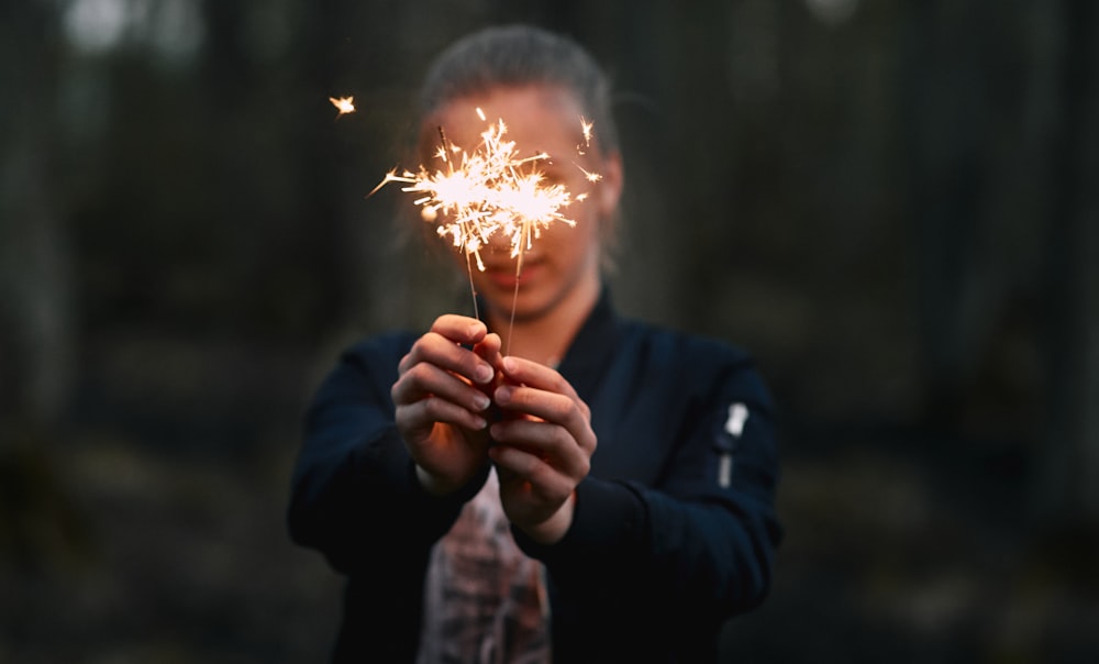 woman holding two lighted sparklers