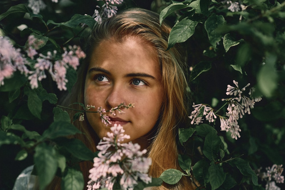 a woman with long blonde hair and blue eyes is surrounded by flowers