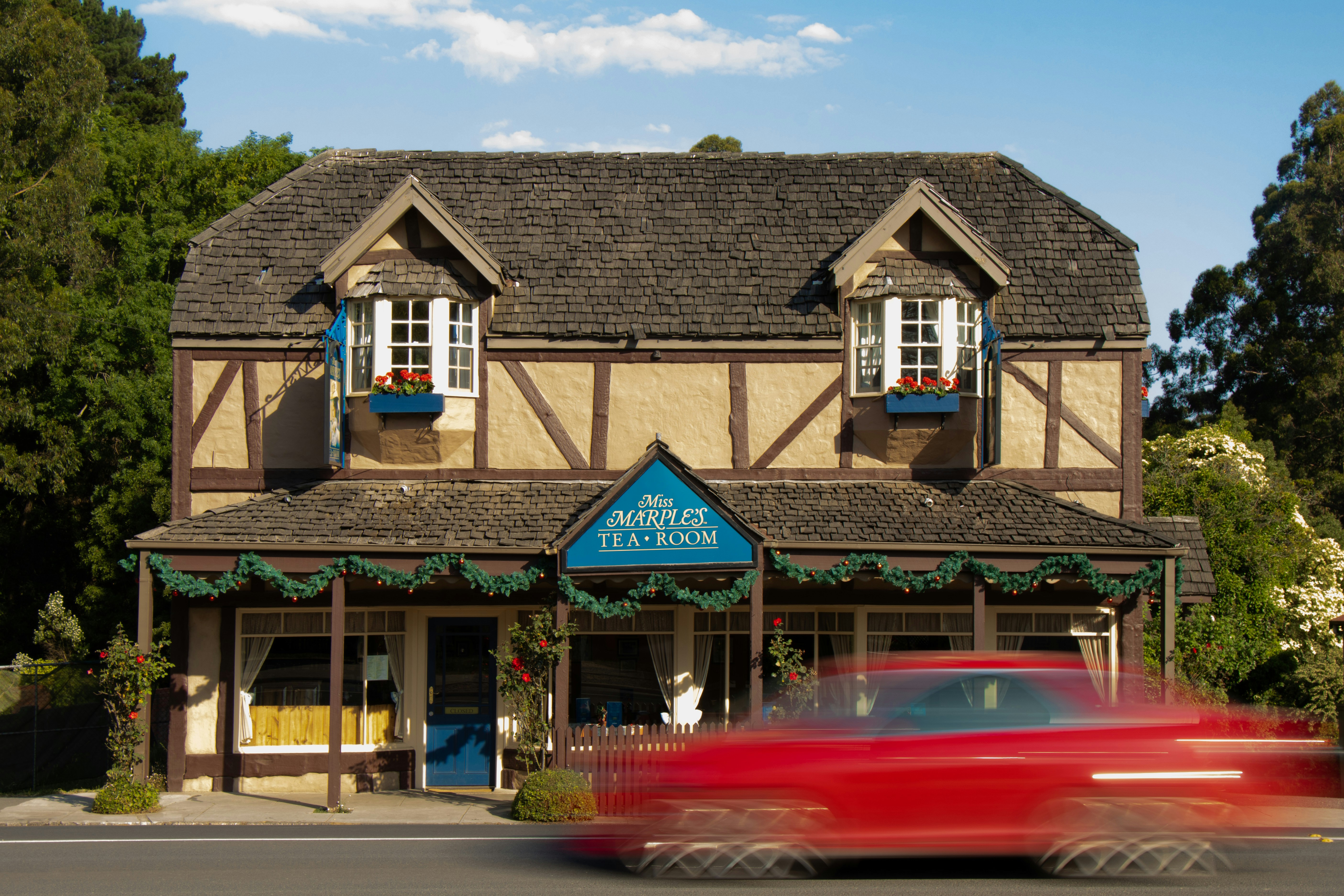 a red car driving past a building with two windows