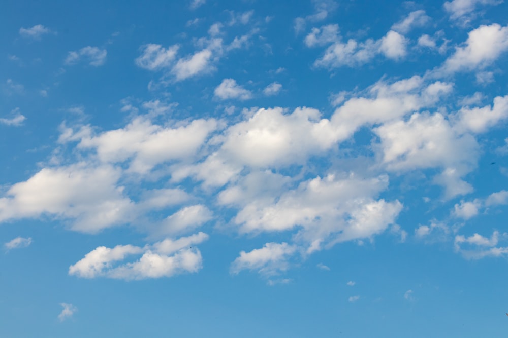 a plane flying through a blue sky with white clouds