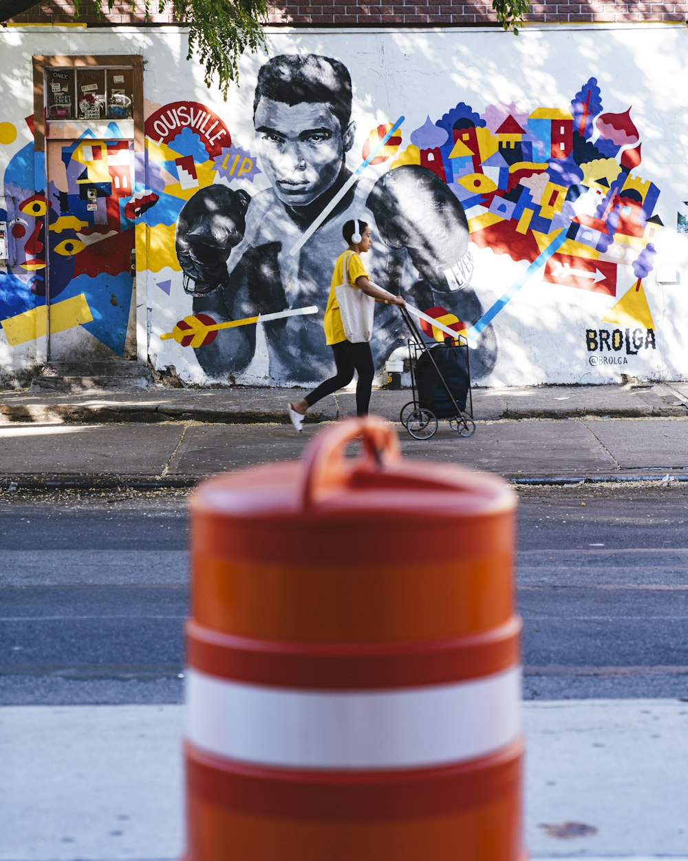 a woman walking down a street past a wall with a painting on it