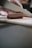 A close-up of a gloved hand slicing a piece of layered cured meat with a sharp knife on a cutting board. The meat displays distinct layers of fat and muscle, indicating it might be bacon or pancetta.