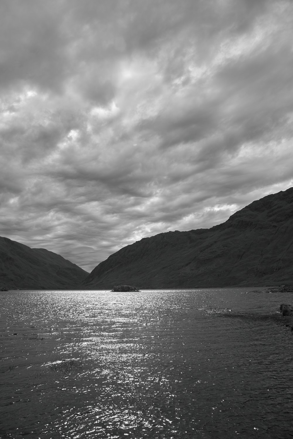 a body of water surrounded by mountains under a cloudy sky