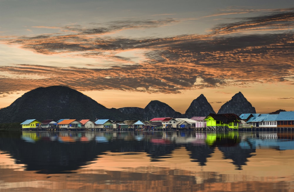 casas de colores variados cerca del cuerpo de agua que ve la montaña bajo el cielo naranja y gris