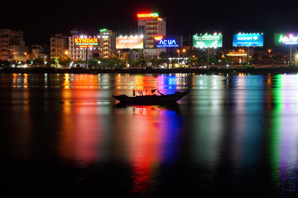 boat on body of water viewing city with high-rise buildings during night time