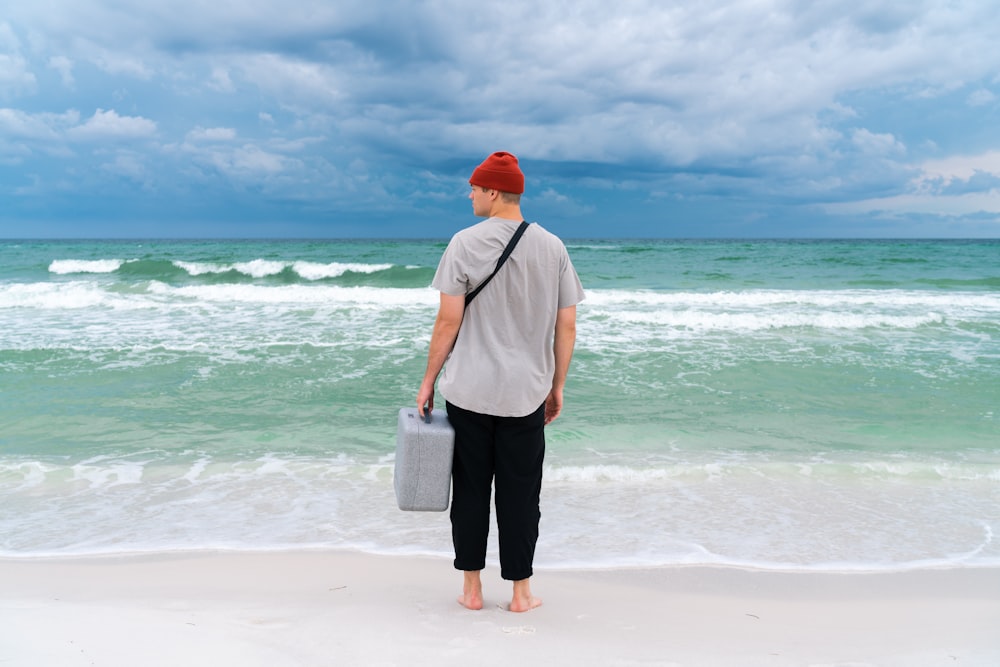 man carrying plastic case standing on seashore during day