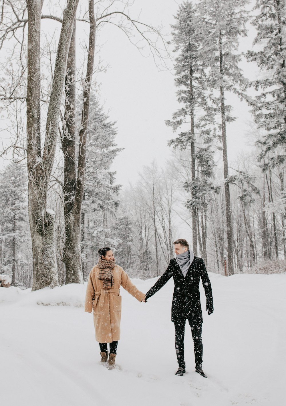 Hombre y mujer tomados de la mano en un campo de nieve cerca de los árboles durante el día