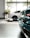 Two luxury cars are parked inside a well-lit showroom with large windows and a view of trees outside. The cars appear to have a sleek, modern design, and the setting includes tiled flooring and plants.