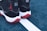 A pair of black and white sneakers with red soles placed on a blue outdoor sports court. The shoes feature a distinct red silhouette logo on the back. The court shows a white line separating two sections.