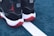 A pair of black and white sneakers with red soles placed on a blue outdoor sports court. The shoes feature a distinct red silhouette logo on the back. The court shows a white line separating two sections.