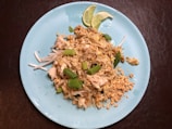 Steaming plate of pad thai noodles garnished with crushed peanuts and lime.