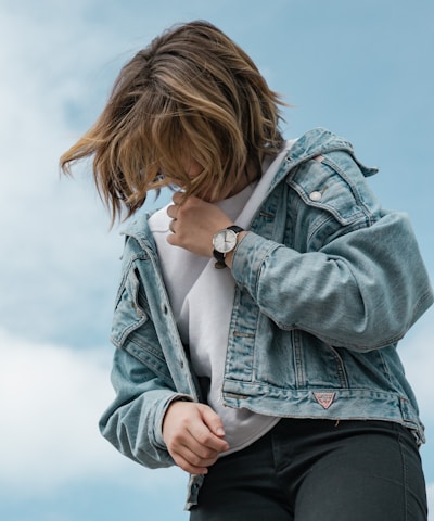 woman wearing white crew-neck t-shirt and blue denim jacket standing while looking down