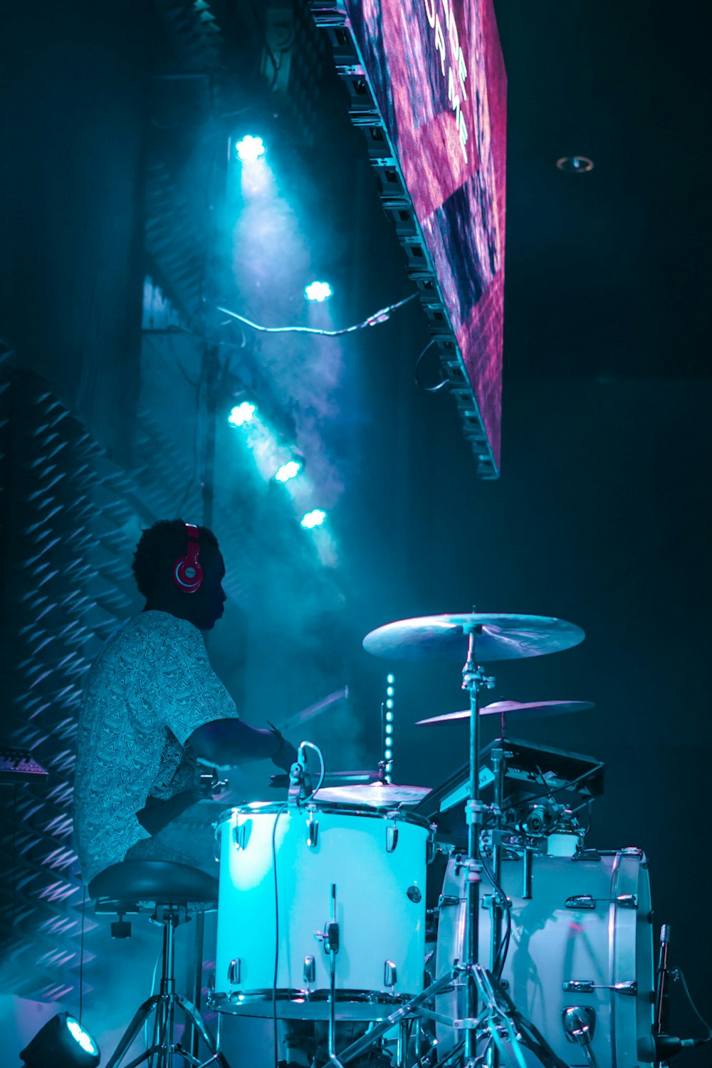 man wearing white and gray t-shirt using red headphones while playing drums