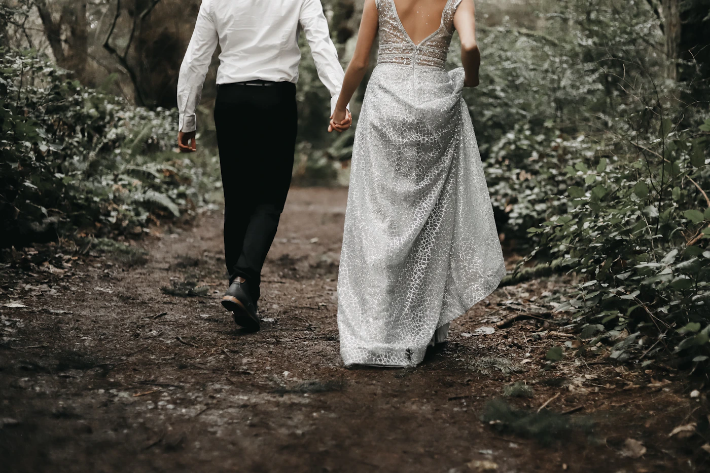 Newlywed couple walking together along a path through a dense green forest with tall trees