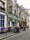 A charming Parisian street café with vintage appeal features purple tables and chairs aligned outside. Climbing vines decorate the building's exterior, and colorful flowers add a welcoming touch.