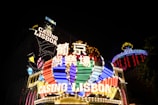 Bright neon signs in multiple colors illuminate the night, prominently displaying the name 'Casino Lisboa' alongside signage in Chinese characters. The lights form intricate patterns and vibrant displays, creating a lively and energetic atmosphere.