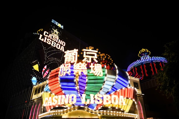 Bright neon signs in multiple colors illuminate the night, prominently displaying the name 'Casino Lisboa' alongside signage in Chinese characters. The lights form intricate patterns and vibrant displays, creating a lively and energetic atmosphere.