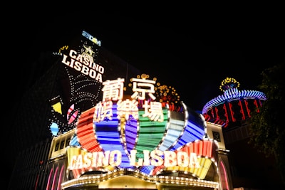 Bright neon signs in multiple colors illuminate the night, prominently displaying the name 'Casino Lisboa' alongside signage in Chinese characters. The lights form intricate patterns and vibrant displays, creating a lively and energetic atmosphere.