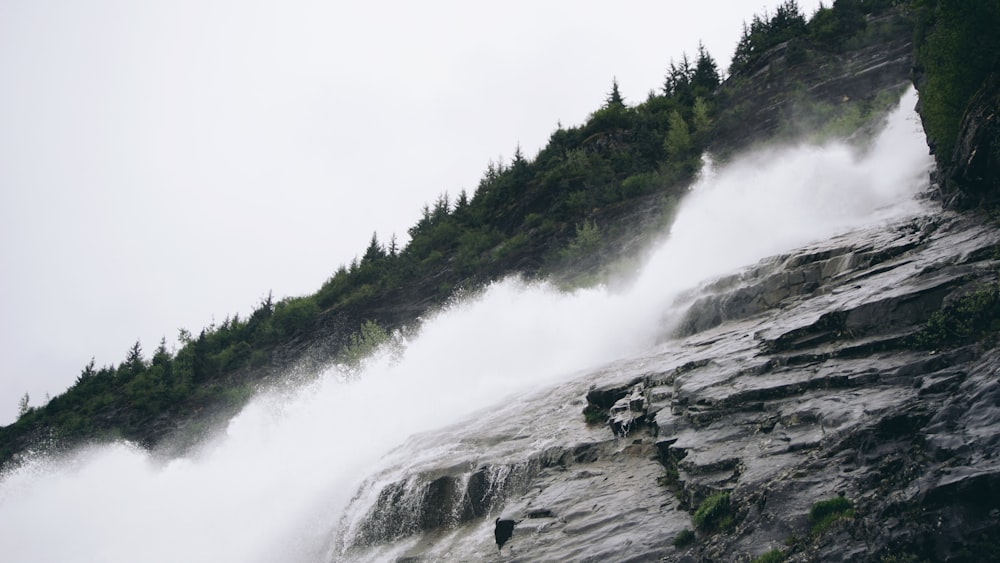 water falls on gray mountain near trees during daytime