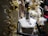 A mannequin is adorned with jewelry, including a necklace and brooch, set against a festive holiday backdrop. The scene is decorated with golden baubles, white garlands, and wrapped gifts with white bows, creating a luxurious and celebratory atmosphere.