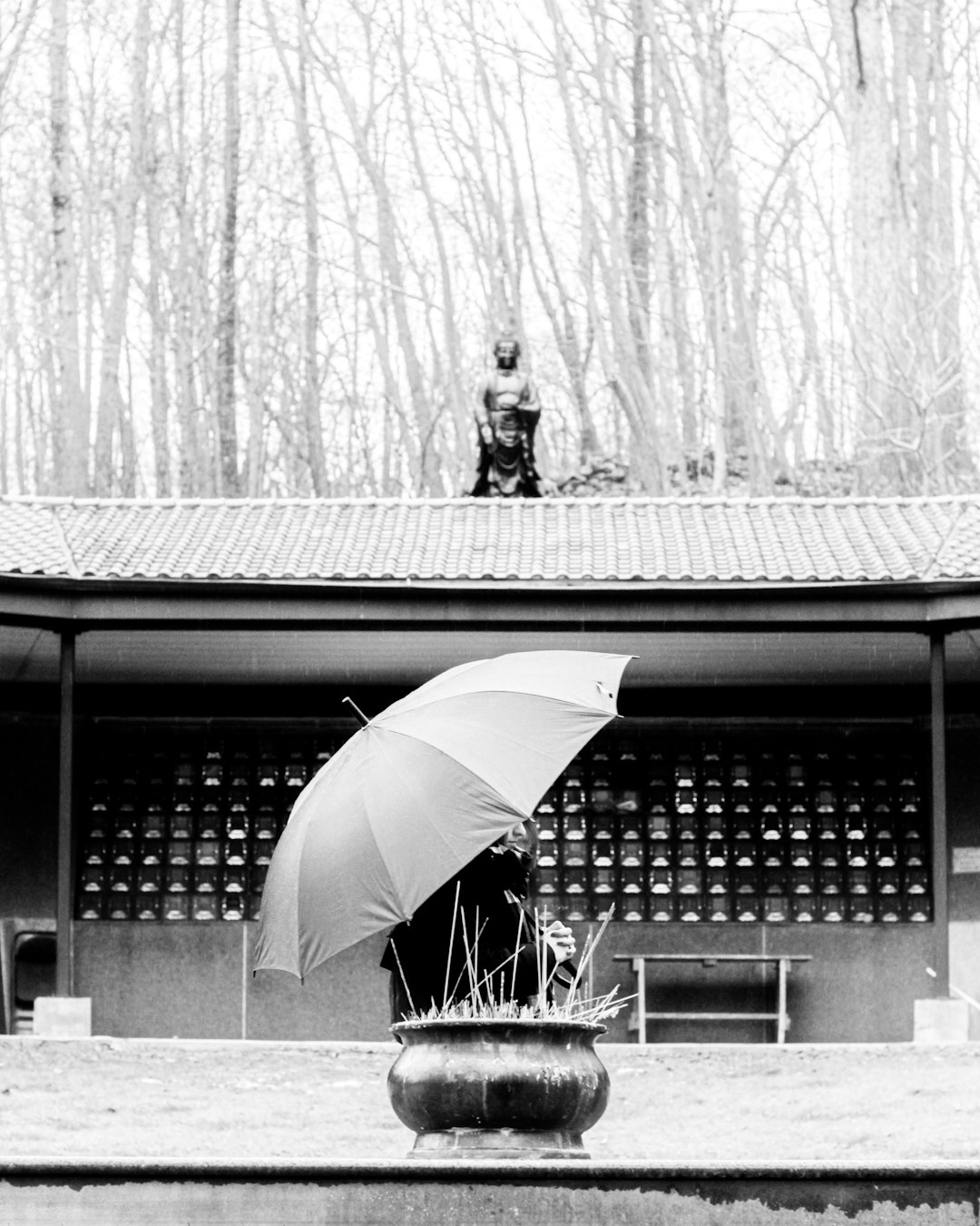 grayscale photography of person using umbrella standing and facing near historic temple