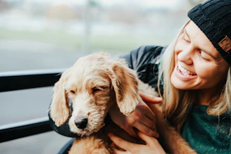 A joyful volunteer gently holding a rescued dog with a bright smile in a sunny outdoor shelter.