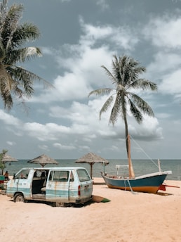 green van near green and brown boat on seashore under white and blue sky