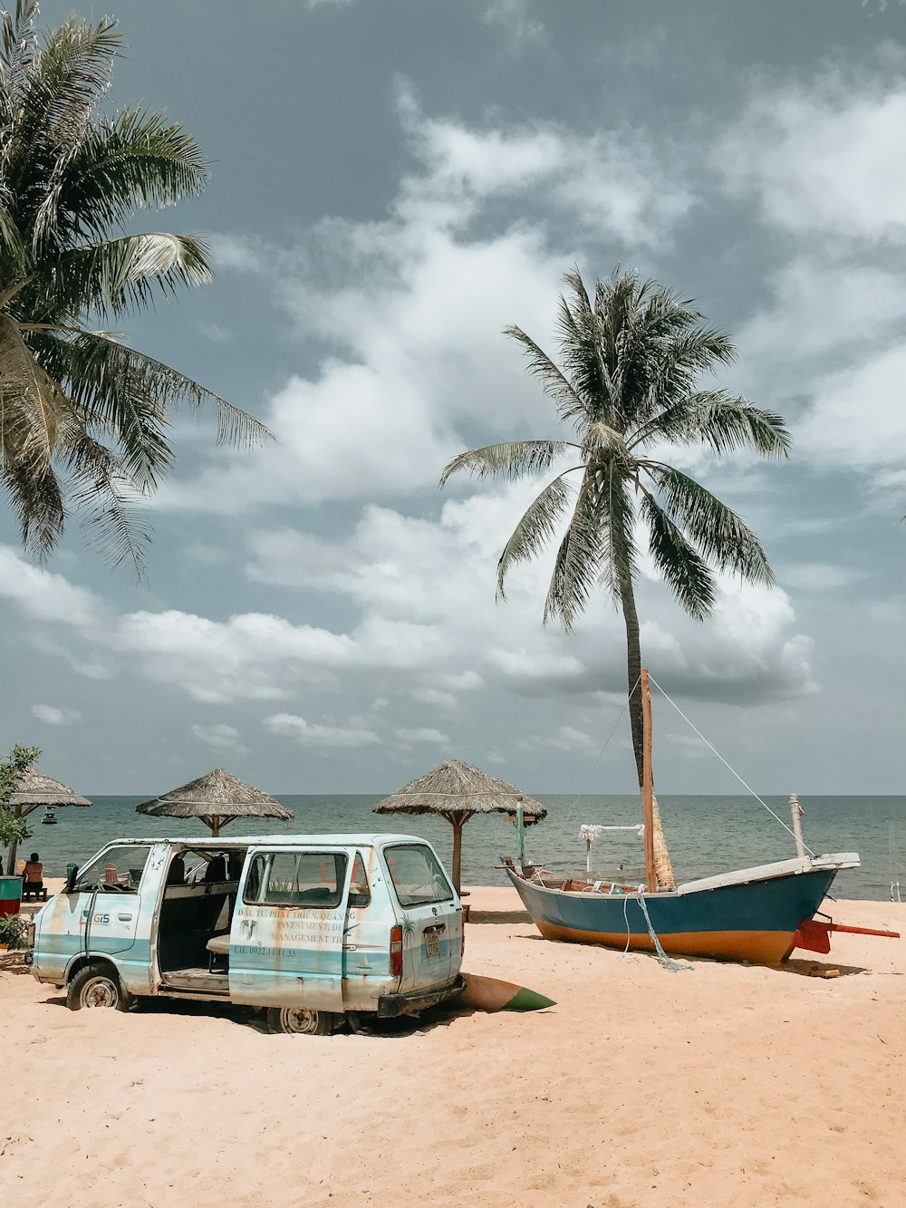 green van near green and brown boat on seashore under white and blue sky