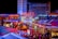 A brightly lit urban scene featuring the entrance to Bally's Las Vegas, surrounded by various illuminated shop signs including Giordano's, Wahlburgers, and Redneck Riviera. The street is bustling with people and rich with neon lights and colorful signage, creating a lively nighttime atmosphere.