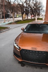 A white Audi A8 with tinted windows driving through a city street lined with trees.