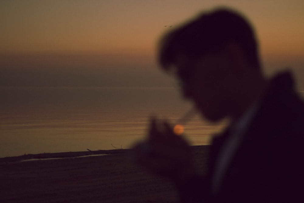 man standing while smoking cigarette near body of water