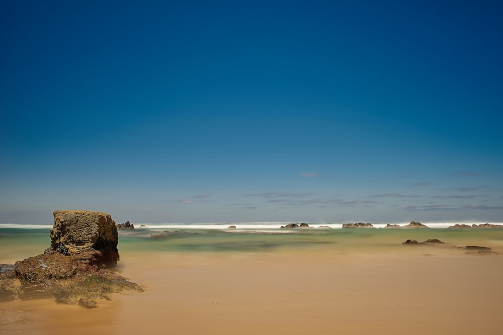 una grande roccia che spunta dalla sabbia su una spiaggia
