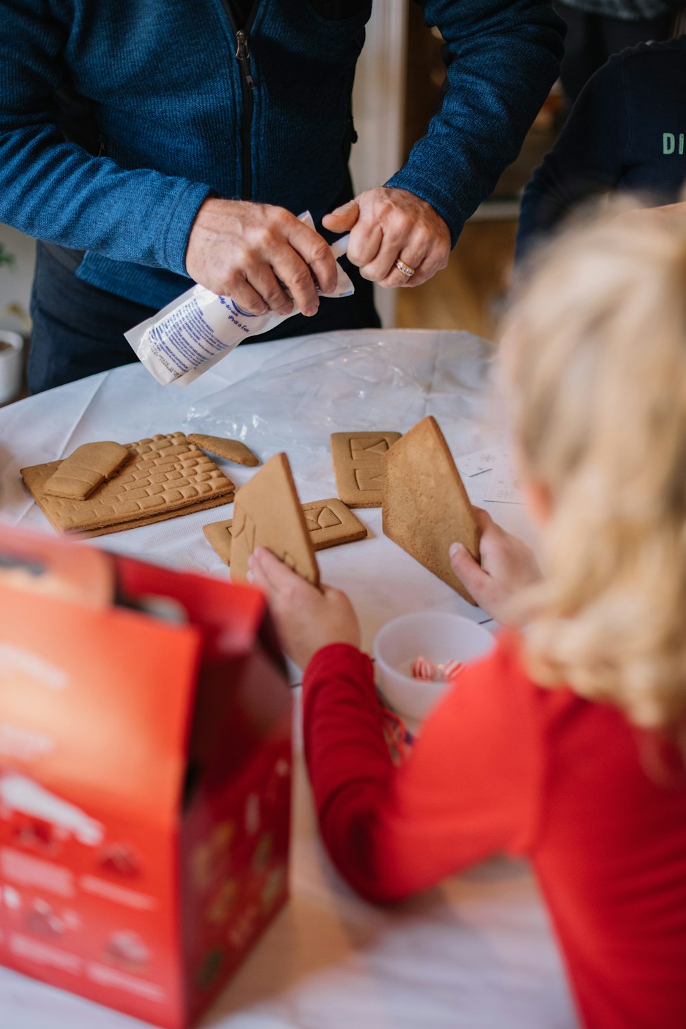 child holding crackers and another person holding whipped cream while standing