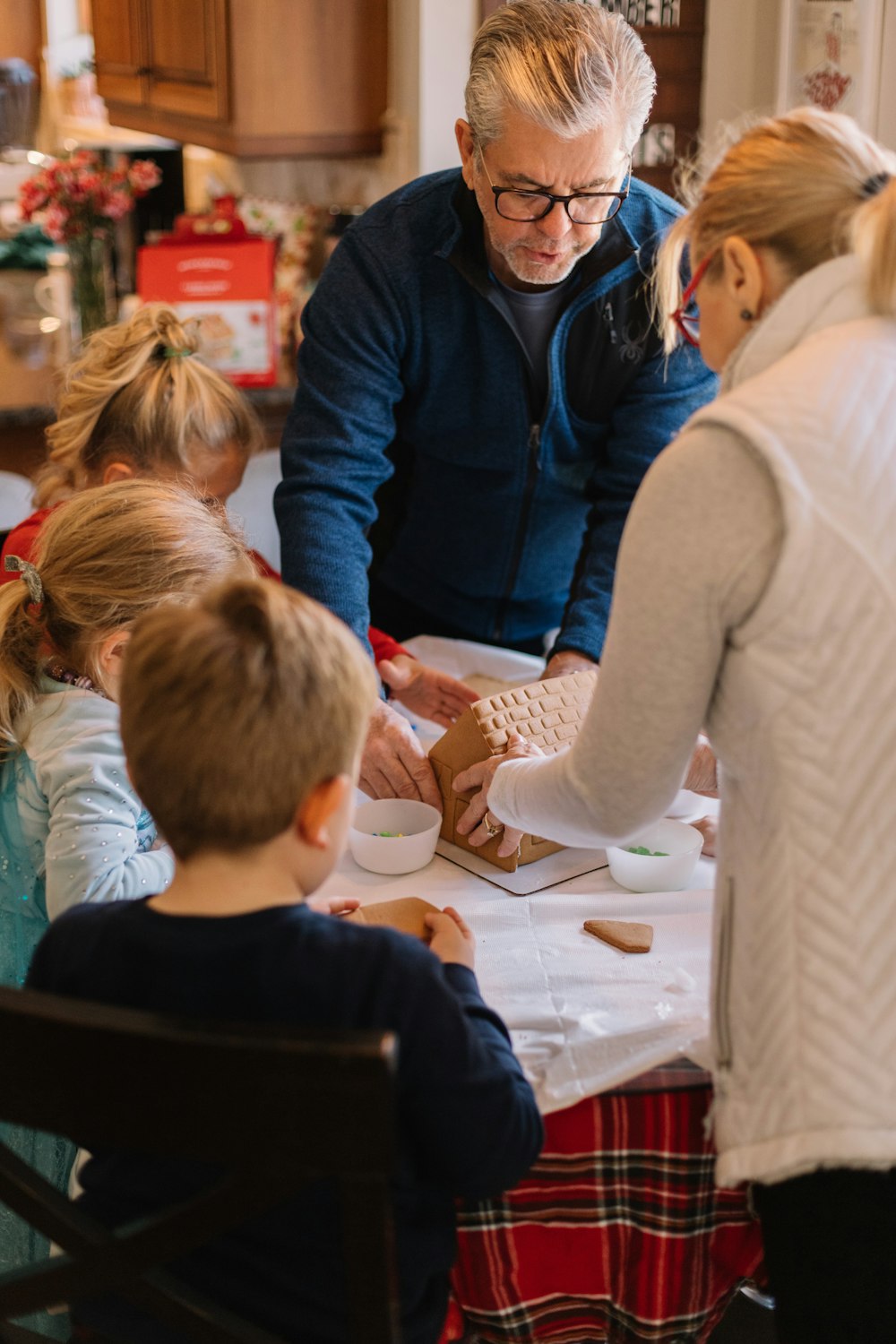 zwei Frauen stehend und drei Kinder sitzend, während sie das Lebkuchenhaus vorbereiten