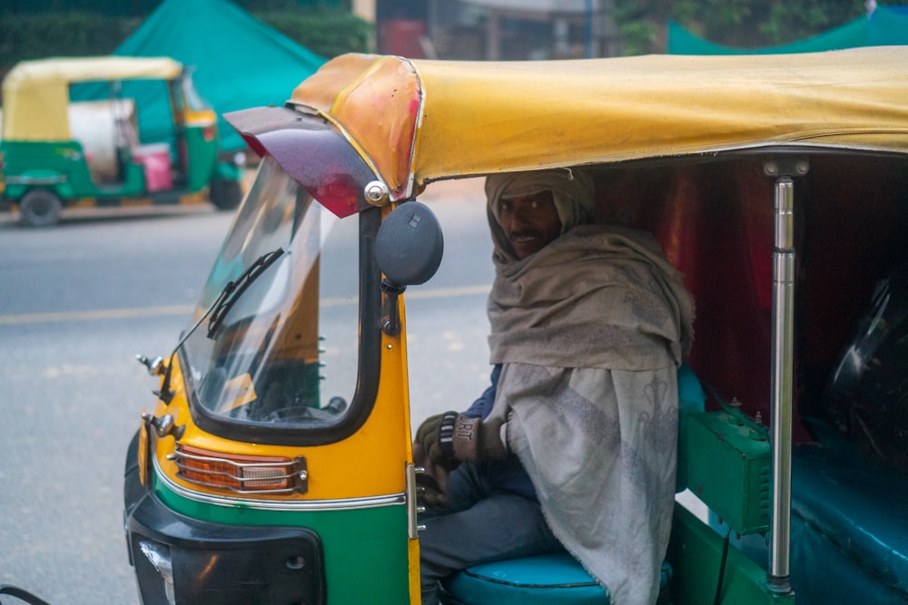 man sitting inside yellow and green autorickshaw