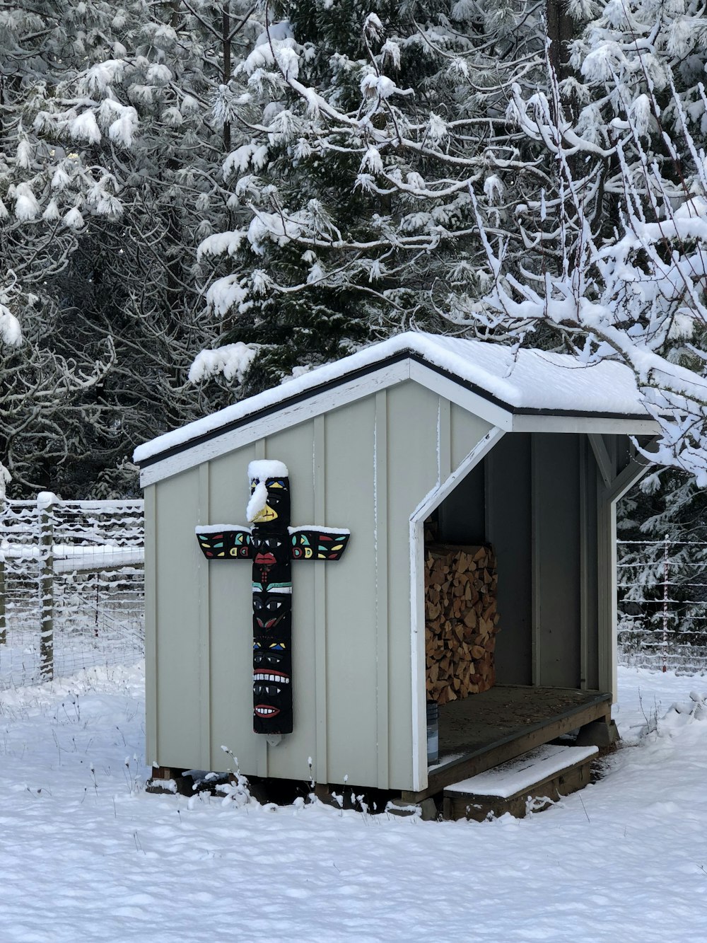 black and multicolored wooden totem on wooden shed surrounded with trees covered with snow